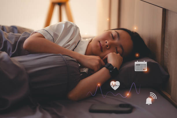 self-development-habit-tracking-apps-with-Asian woman wearing smartwatch for tracking sleep rate showing icon by hologram virtual, resting with technology in bed room at night.